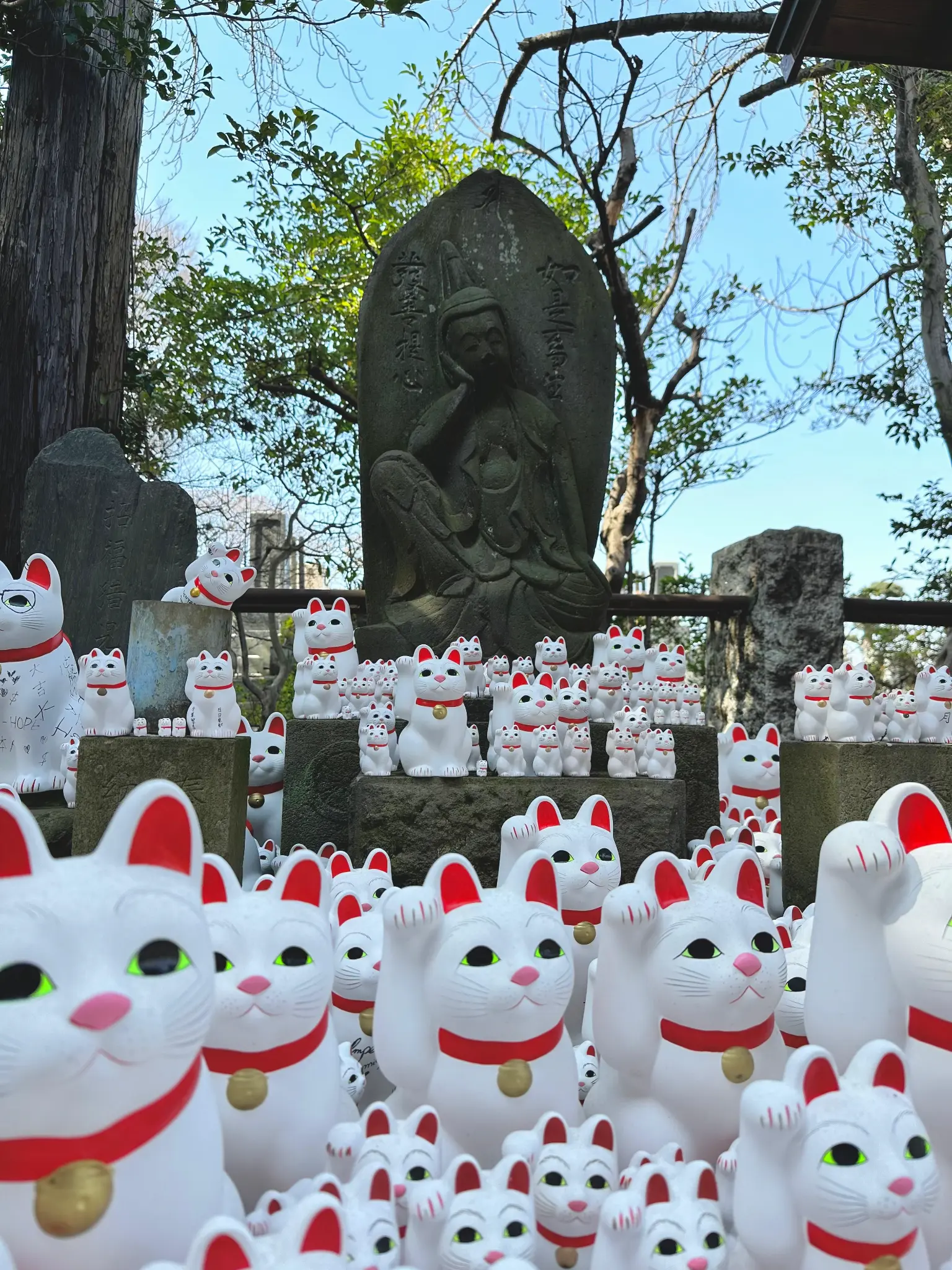 Maneki-neko statues with a Buddha statue in the background at Gotokuji Temple