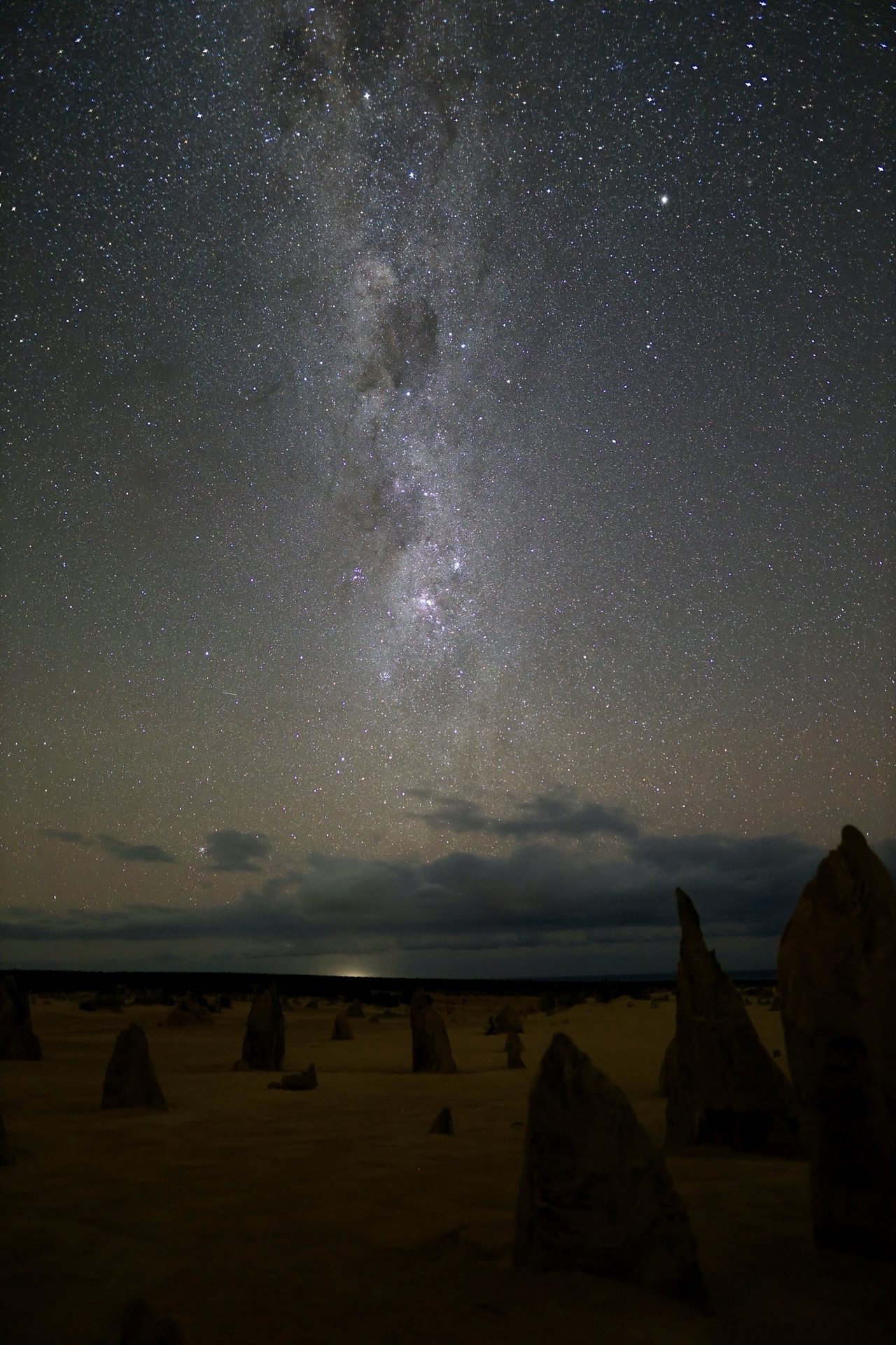 The complete Milky Way galaxy stretching from top to bottom of the frame above the Pinnacles Desert, with limestone spires silhouetted in the foreground