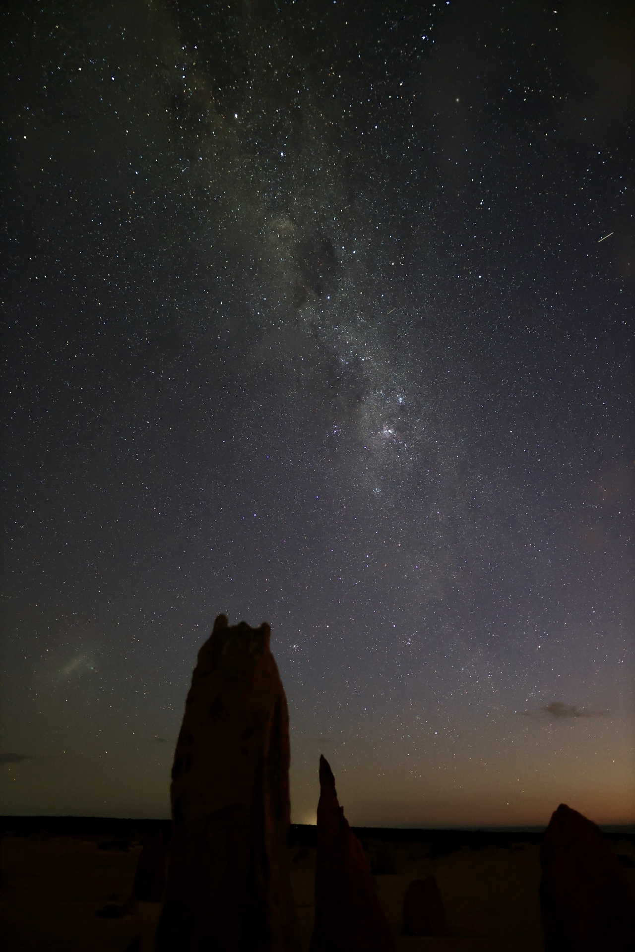 Milky Way galaxy arching over silhouetted limestone pinnacles with the glow of the Indian Ocean visible on the horizon, Nambung National Park