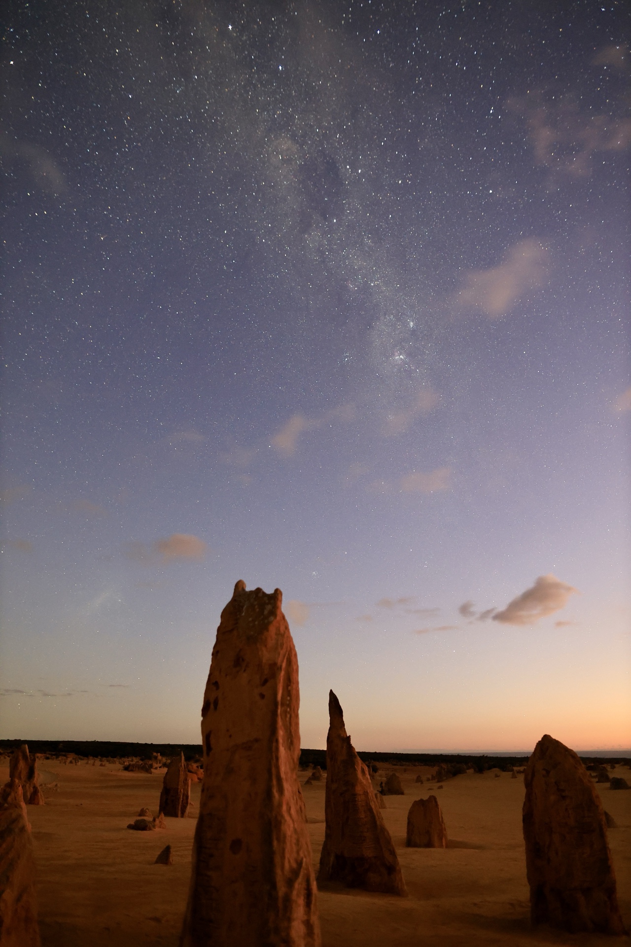 A tall limestone pinnacle silhouetted against a twilight sky with early Milky Way stars visible above the orange horizon glow, Nambung National Park