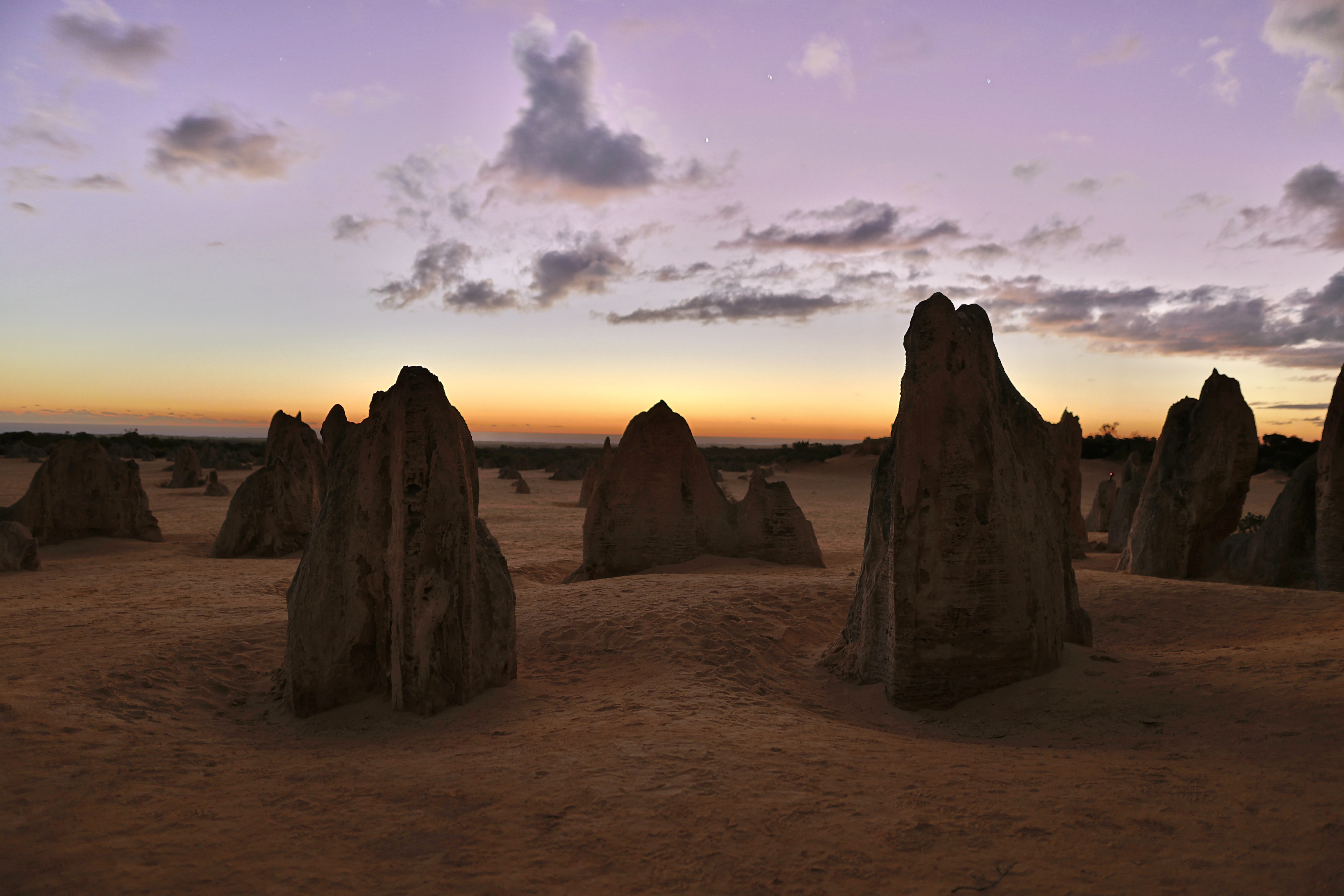 Limestone pinnacle silhouettes against a vivid purple and orange twilight sky at Nambung National Park, Western Australia